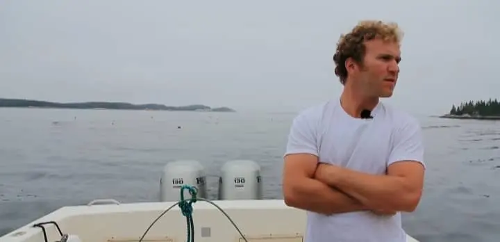 Noah Oppenheim a marine biologist wearing white t shirt stands on a boat with his arm crossed looking to the side.